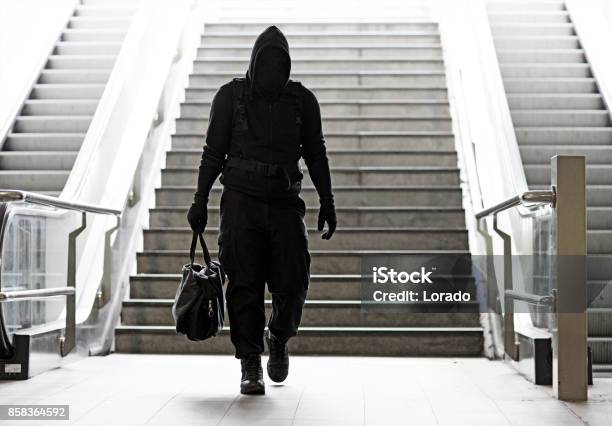 Hooded Lone Wolf Man Wearing Black Carrying Bag In Urban Underground Public Transport Setting Stock Photo - Download Image Now