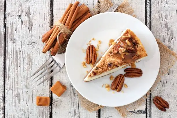 Photo of Slice of pecan caramel cheesecake, top view over white wood