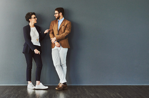 Shot of two designers having a conversation while leaning against a wall