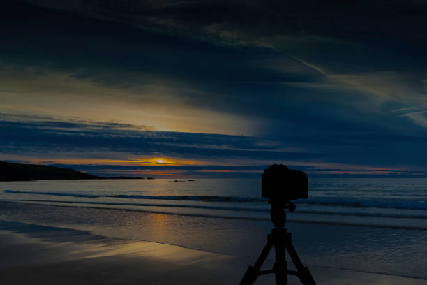 istock Camera on tripod with ocean and sunset in background 858387382