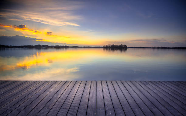 Wooden recreational swimming deck on the lakeside during spectacular sunset over water. Ready for product montage display.