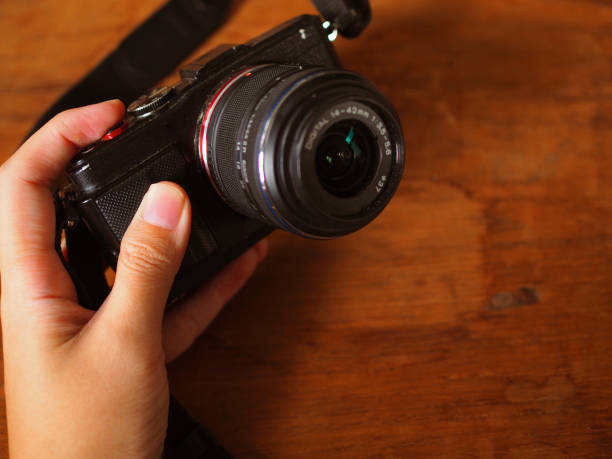 istock Hand holding black camera, wooden background 858430422