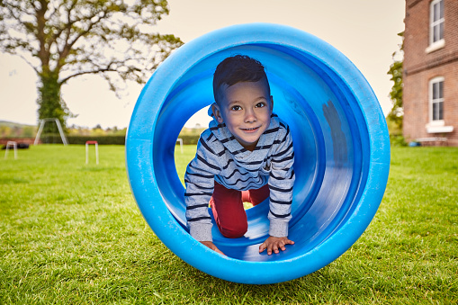 Cute little boy playing inside a toy tunnel in backyard lawn