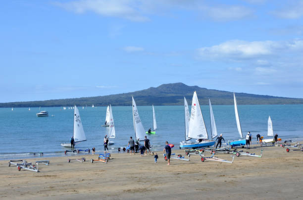 Sail boats on Narrow Neck Beach against Rangitoto island Auckland AUCKLAND - SEP 24 2017: Sailors sail boats in Narrow Neck Beach against Rangitoto island, a volcanic island in the Hauraki Gulf and iconic landmark of Auckland, New Zealand. rangitoto island stock pictures, royalty-free photos & images