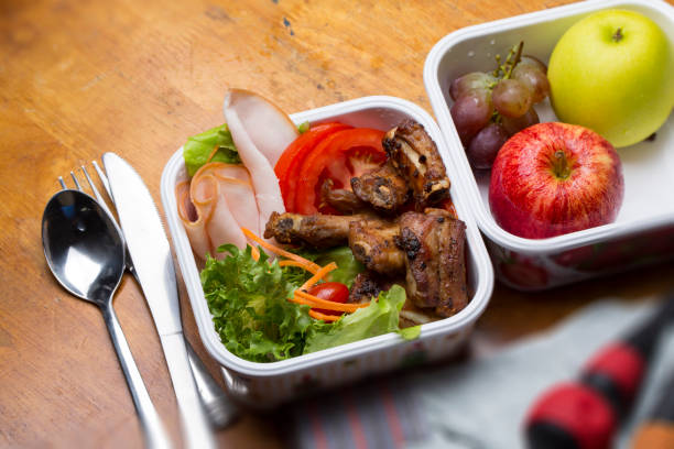 istock Well Prepared Lunch Box, Including Marinated pork ribs Fried, Fresh Vegetable, Grapes,Red and Green Apple in White Box, Placed on Wooden table. Concept of Healthy food for who working in the field like mechanic or electrician. 858503218