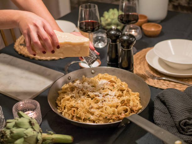 mão de mulheres esfregando ralar queijo parmesão com ralador. macarrão na panela em uma configuração de mesa de jantar. - food and drink cheese grated bowl - fotografias e filmes do acervo