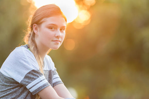 Portrait of pretty Caucasian preteen girl with the sun setting in the background. Copy space available.