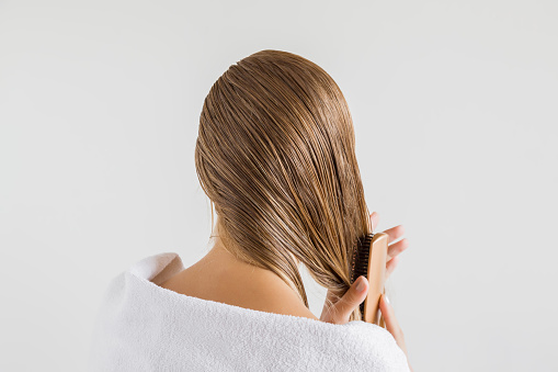 Mujer en la toalla blanca con peine cepilla su pelo rubio mojado después de la ducha sobre el fondo gris. Se preocupa por un cabello sano y limpio. Concepto de salón de belleza. photo