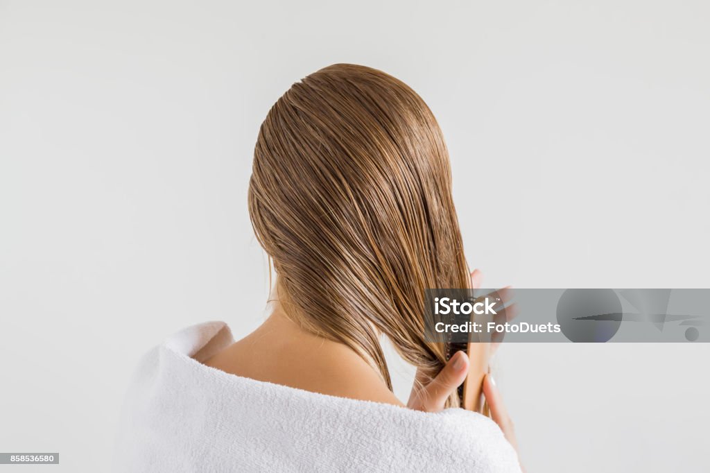 Mujer en la toalla blanca con peine cepilla su pelo rubio mojado después de la ducha sobre el fondo gris. Se preocupa por un cabello sano y limpio. Concepto de salón de belleza. - Foto de stock de Pelo libre de derechos