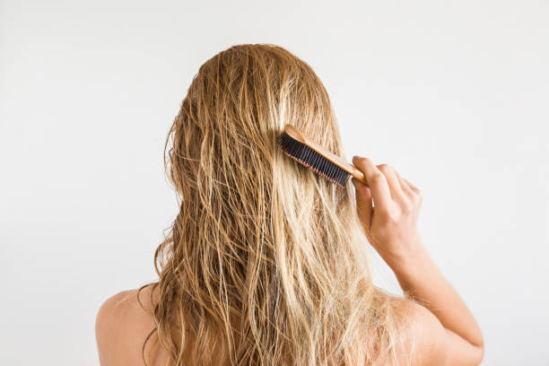 mujer con peine cepilla su pelo rubio mojado después de la ducha sobre el fondo gris. se preocupa por un cabello sano y limpio. concepto de salón de belleza. - hair care combing women human hair fotografías e imágenes de stock