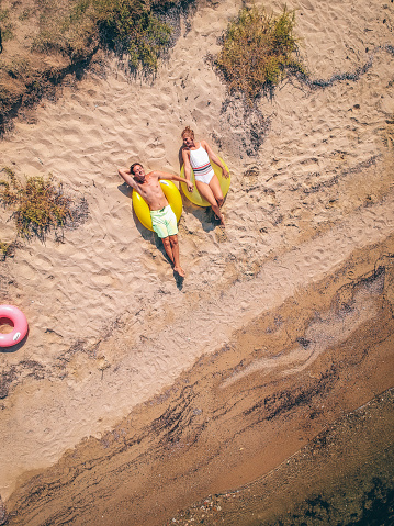Aerial view photo of an young couple, lying down on the sand, sunbathing and enjoying their vacation