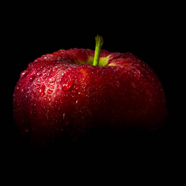 Water droplet on glossy surface of red apple on black background