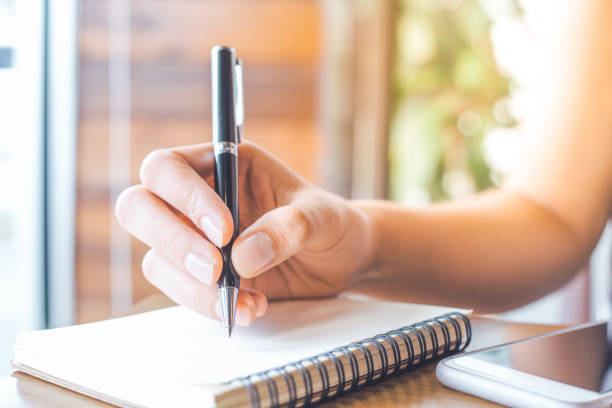 istock woman's hand is writing on a blank notepad with a pen on a wooden desk. 858579594