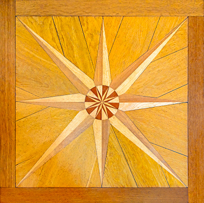 Marquetry or intarsia on parquet flooring. Crafted wind rose on beautiful woodworks. Star shape symbol within a wooden frame.