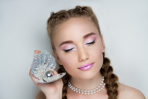 Young beautiful woman girl lady holds a large sink with silver pearl. model fashionable hairdo, professional makeup pink color trendy lips. Closeup horizontal photo face. gray background free place