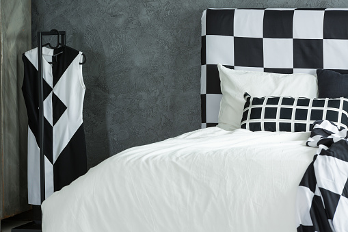 Black and white fashion dress on hanger in bedroom with patterned bedhead and pillow on bed against textured wall