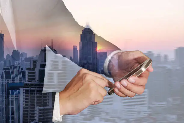 Photo of Double exposure of business man hand tuoch touch screen smart phone, cellphone, sunset and citys on motion abstract city in the evening background as Technology and communication concept.