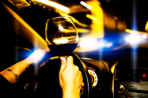 Motor vehicle driver drives a car holding a glass of wine.  Drinking and  driving is both  illegal and dangerous.