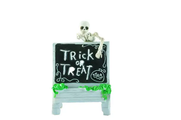Photo of Halloween concept : Plastic human skeleton model climbing on dirty ceramic Trick or Treat sign isolated on white background