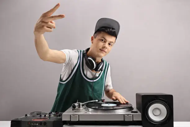 Teenage DJ making a peace sign against a gray wall