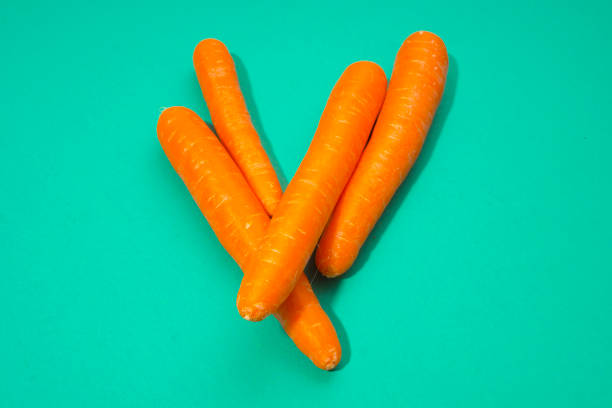 Orange carrots on green paper background, minimalist still life