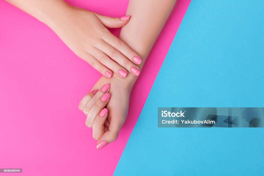 Closeup of hands of a young woman with manicure on nails against pink background Pink Color Stock Photo