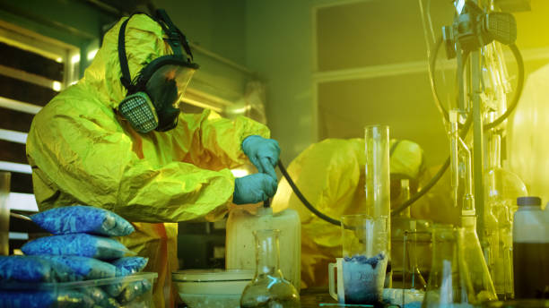 en el laboratorio de drogas subterráneo dos químicos clandestinos con monos y máscaras de protección utilizan manguera para la destilación de la droga. se cocinan los medicamentos sintetizados en el edificio abandonado. - servicio federal de protección fotografías e imágenes de stock