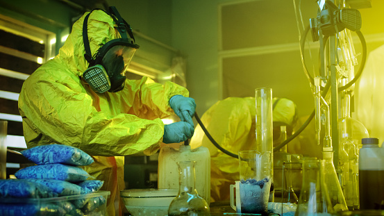 In the Underground Drug Laboratory Two Clandestine Chemists Wearing Protective Masks and Coveralls Use Hosepipe For Drug Distillation. They Cook Synthesised Drugs in the Abandoned Building.
