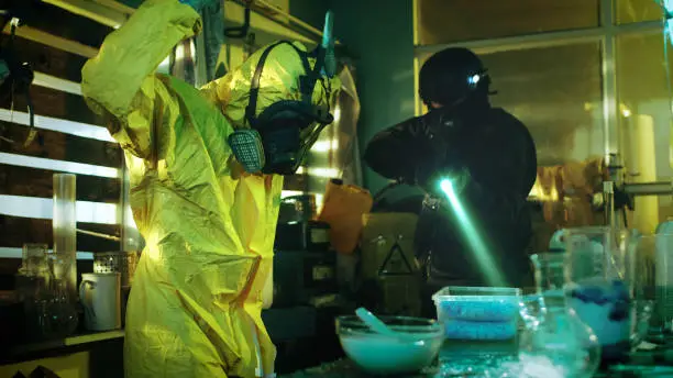 Photo of Fully Armed Special Anti-Narcotics Task Forces Soldier Arrests Clandestine Chemist in the Drug Producing Underground Laboratory. Chemist Raises Hands and Surrenders. A lot of Functional Drug Production Equipment is Standing Around. Shot in Slow Motion.