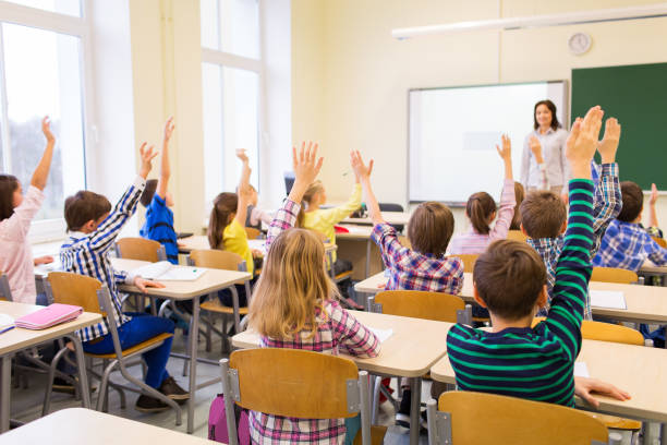 group of school kids raising hands in classroom education, elementary school, learning and people concept - group of school kids with teacher sitting in classroom and raising hands schoolboy stock pictures, royalty-free photos & images