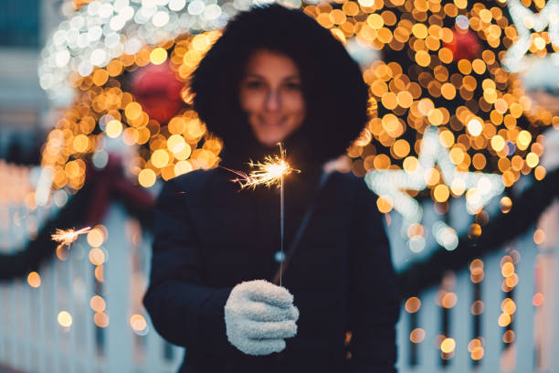 Smiling woman in front of the Christmas tree holding a sparkler