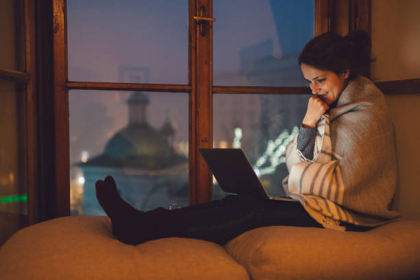 Girl enjoying to be home for Christmas Relaxed woman at the window sill enjoying a movie on the lap top movie scene stock pictures, royalty-free photos & images