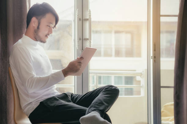 istock Asian men in white t-shirts are using the tablet to work on vacations. 858692376
