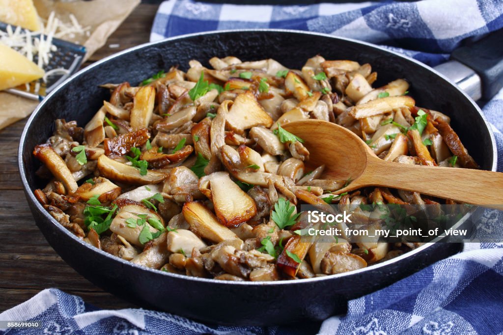 fried porcini with parsley in skillet delicious fried porcini sprinkled with parsley in skillet with wooden spoon on dark wooden table. parmesan cheese, kitchen towel on background, close-up, selective focus Mushroom Stock Photo