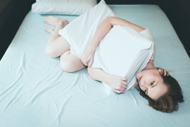 istock Young depressed woman lying down in bed and hugging pillow 858705838