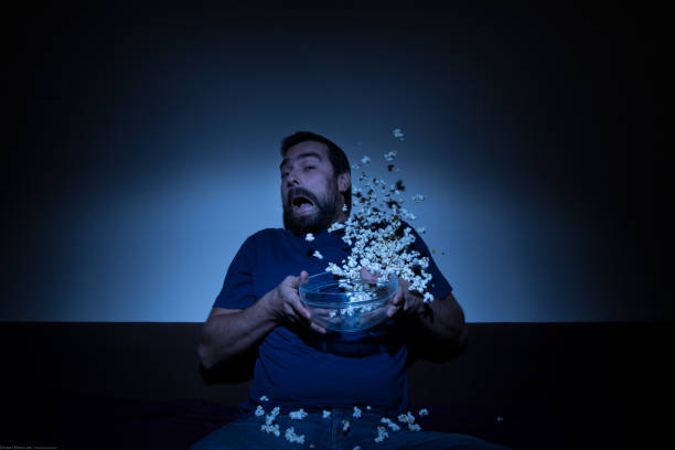 istock Scared man watching a horror movie and jumping with popcorn flying allover 858707638