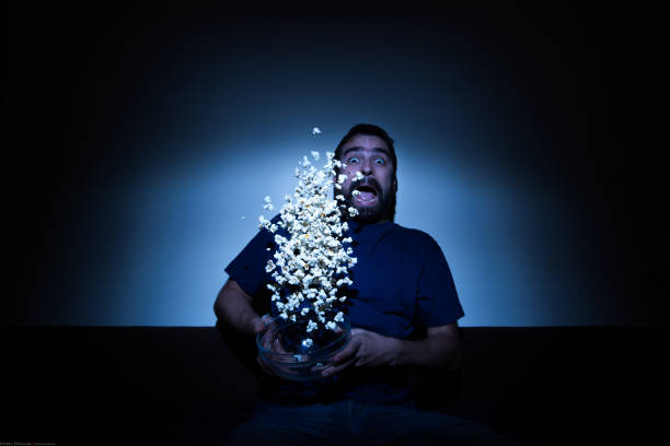 istock Scared man watching a horror movie and jumping with popcorn flying allover 858707718