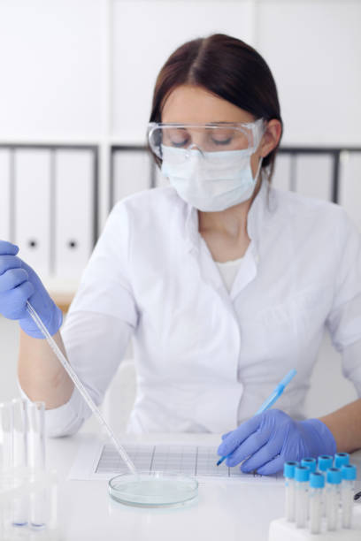 close-up of professional female scientist in protective eyeglasses making experiment with reagents in laboratory. medicine and research concept - close up medical test exam people imagens e fotografias de stock