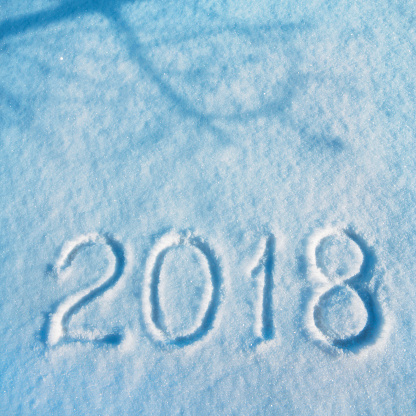 New Year 2018 written on the snow (in blue tones). Close-up DSLR photo with nice real snow texture. Shadow of the tree on the snow. Space for copy.