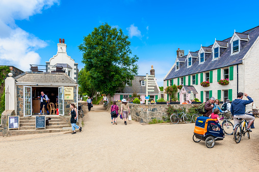 Sark, United Kingdom - July 5, 2013: Unpaved street with restaurants and tourists in The Village, the center of Sark, Channel Islands, UK. No cars or trucks are allowed on Sark so walking or cycling is the only option.