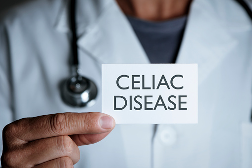 closeup of a young caucasian doctor man in a white coat showing a signboard with the text celiac disease written in it