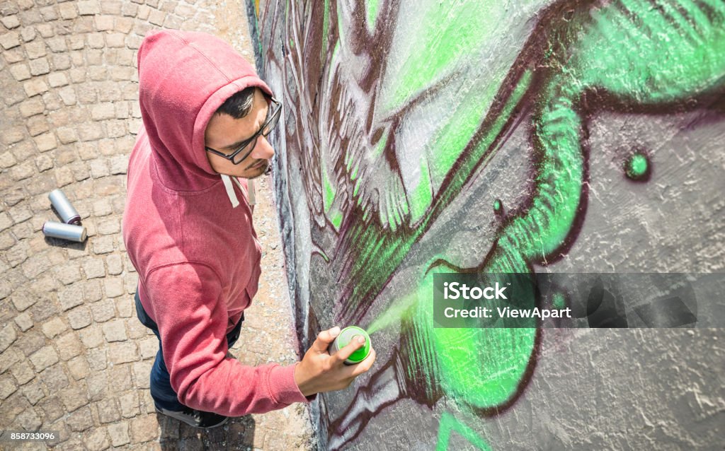 Street artist painting colorful graffiti on generic wall - Modern art concept with urban guy performing and preparing live murales with green aerosol color spray - Sunny afternoon neutral filter Graffiti Stock Photo