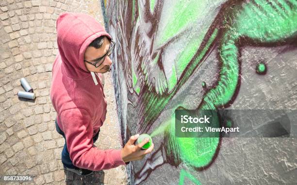 Street Artist Painting Colorful Graffiti On Generic Wall Modern Art Concept With Urban Guy Performing And Preparing Live Murales With Green Aerosol Color Spray Sunny Afternoon Neutral Filter Stock Photo - Download Image Now