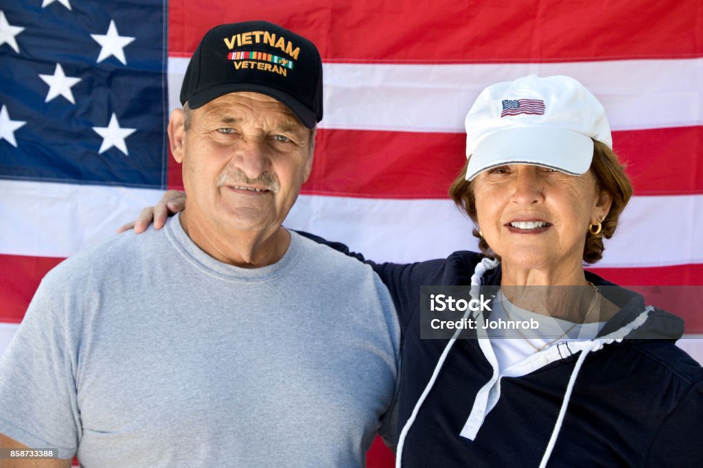 Vietnam Veteran and Wife looking at camera with American Flag in background Image shot with Canon Rebel T6s 24 Megapixel, 24-105mm f/4L IS USM lens. Veteran Stock Photo