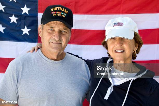 Vietnam Veteran And Wife Looking At Camera With American Flag In Background Stock Photo - Download Image Now