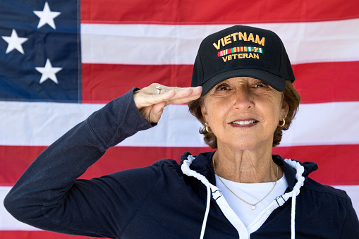 Mujer Vietnam veterano saludando mirando contenido usa tapa de veteranos, con bandera estadounidense de fondo. photo