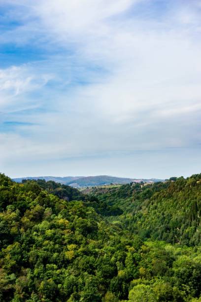 istock Vertical photo with view into the small valley between two hills or rocks covered by green forest in Italy Tuscany. The sky is partially blue but mainly covered by white clouds. 858741612