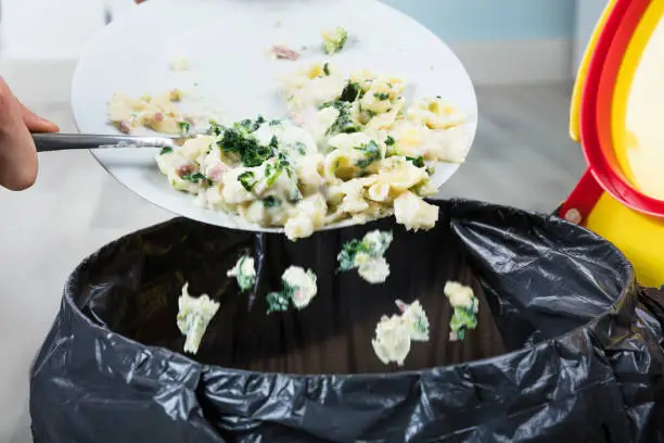 Close-up Of A Person Throwing The Leftover Pasta Into The Trash Bin