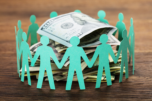 Crowdfunding Concept. Paper Cut Out Human Figures Around The Stack Of Hundred Dollar Bills