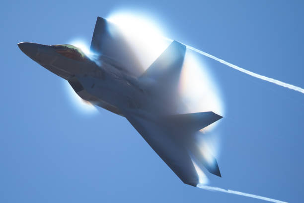 Photo of Military Airplane in a high-G maneuver, with afterburners on, and condensation clouds and streaks around the plane..